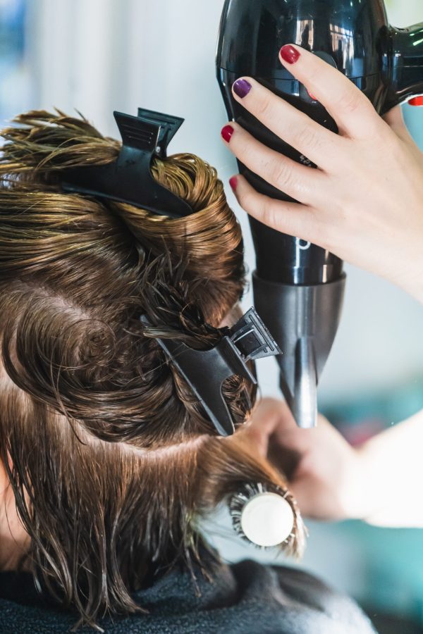 A vertical closeup shot of a hairdresser blow drying a woman's short hair in a beauty salon